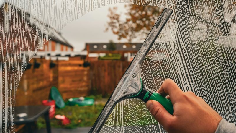 Squeegee wiping sparkling clean window glass with sunlight streaming through